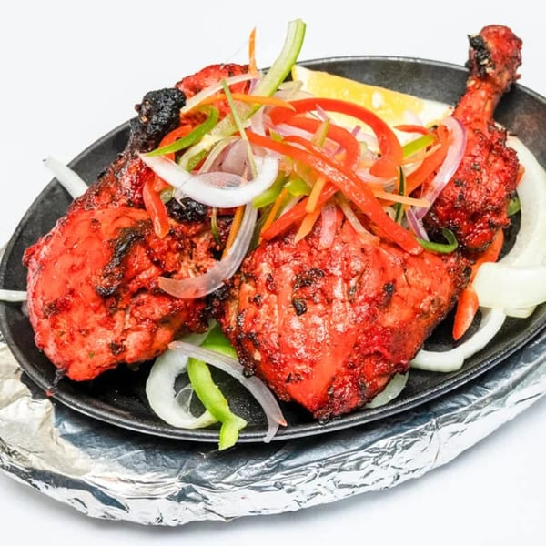 Neelam Indian Cuisine's Tandoori Chicken, garnished with sliced onions, bell peppers, and a lemon wedge.