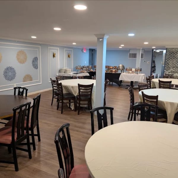 Neelam Indian Cuisine's dining room with round tables, chairs, and a buffet setup against light blue walls.