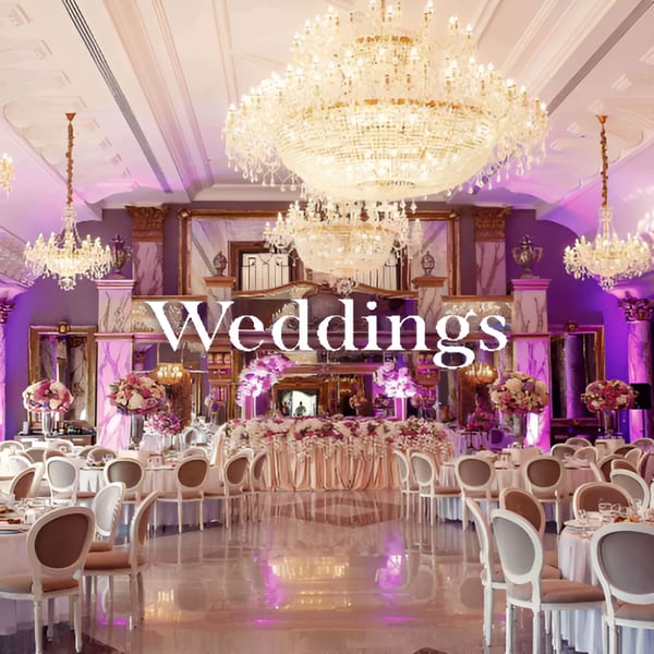 Elegant wedding reception hall with chandeliers, purple lighting, and tables set for guests.