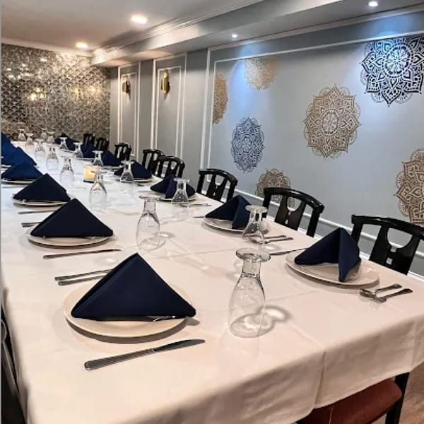 A long dining table set with white tablecloths, blue napkins, and glassware at Neelam Indian Cuisine.