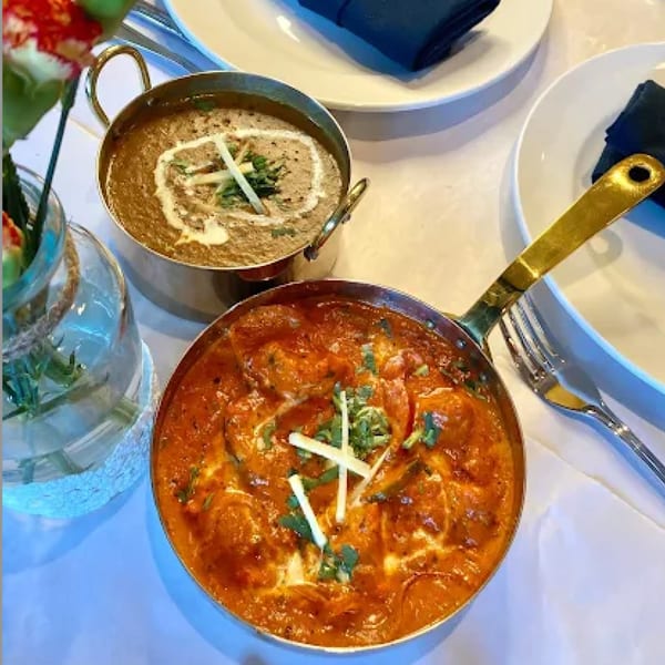 Two Indian dishes, one orange curry and one brown lentil dish, on a white tablecloth.