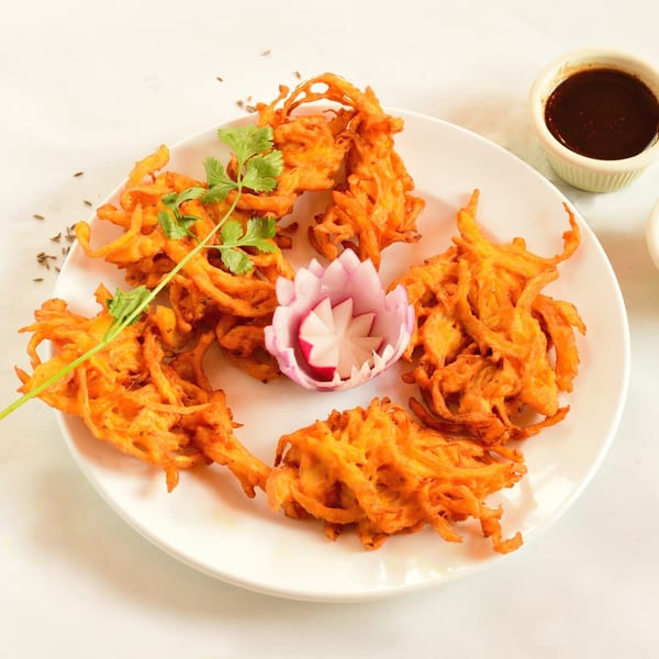 Crispy Indian onion bhaji pakora, garnished with cilantro and a carved radish, served with dipping sauce.