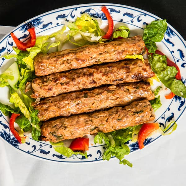 Four Seekh Kebabs from Neelam Indian Cuisine, garnished with fresh lettuce, cucumber, and red bell pepper.