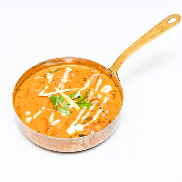 Neelam Indian Cuisine's butter chicken, garnished with cream swirls, ginger, and cilantro in a copper pan.