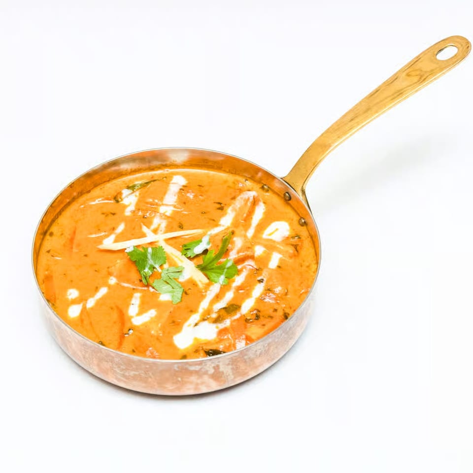 Neelam Indian Cuisine's butter chicken, garnished with cream swirls, ginger, and cilantro in a copper pan.
